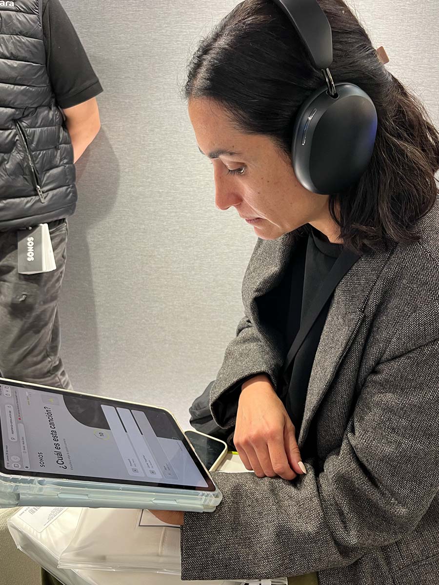 Participante con audífonos Sonos responde en el iPad la pregunta ¿cuál es esta canción? durante una partida